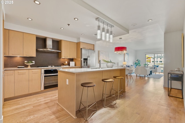 kitchen with wall chimney range hood, appliances with stainless steel finishes, light brown cabinets, and tasteful backsplash