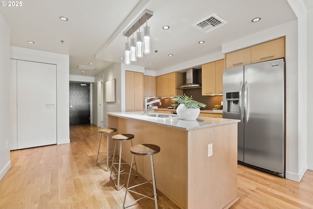 kitchen featuring a sink, light wood finished floors, stainless steel fridge with ice dispenser, wall chimney exhaust hood, and visible vents