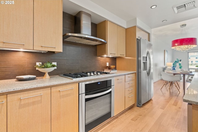 kitchen with wall chimney range hood, light brown cabinetry, appliances with stainless steel finishes, light wood-style flooring, and visible vents