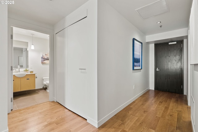 hallway featuring a sink, light wood-style floors, recessed lighting, baseboards, and visible vents