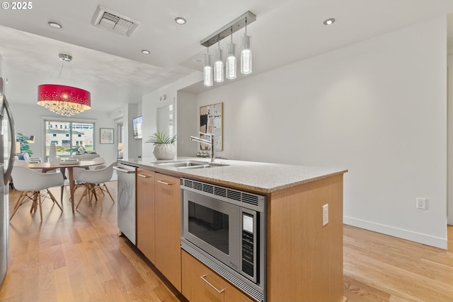 kitchen with visible vents, an island with sink, a sink, light wood finished floors, and stainless steel appliances