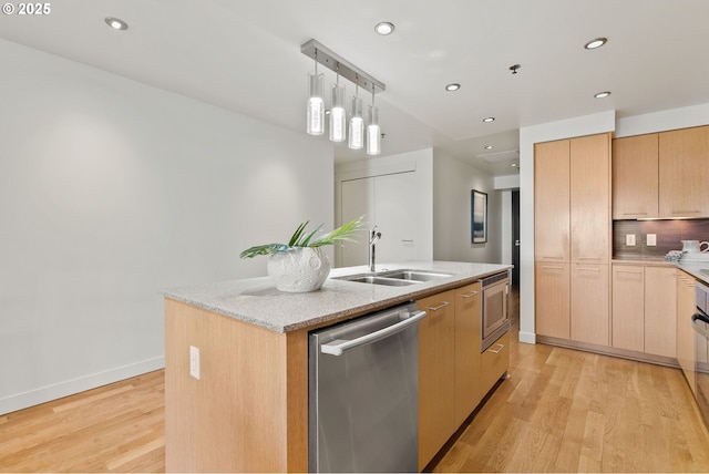 kitchen featuring light stone countertops, a center island with sink, a sink, light wood-style flooring, and appliances with stainless steel finishes