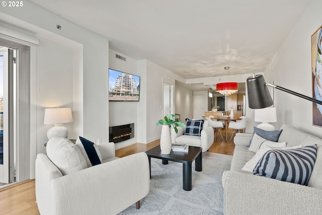 living room featuring baseboards, a glass covered fireplace, wood finished floors, and visible vents