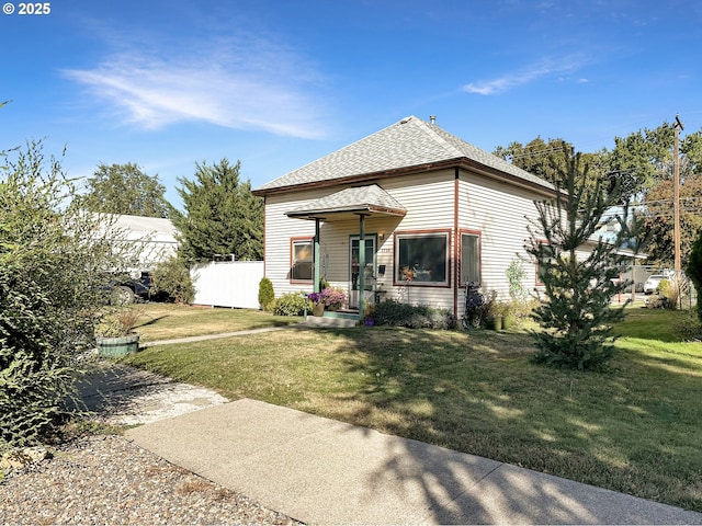 rear view of property featuring fence, a lawn, and roof with shingles