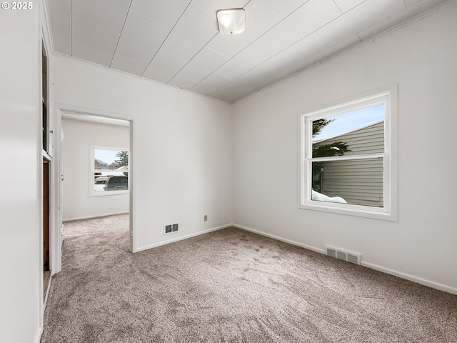 carpeted empty room featuring plenty of natural light, visible vents, and baseboards