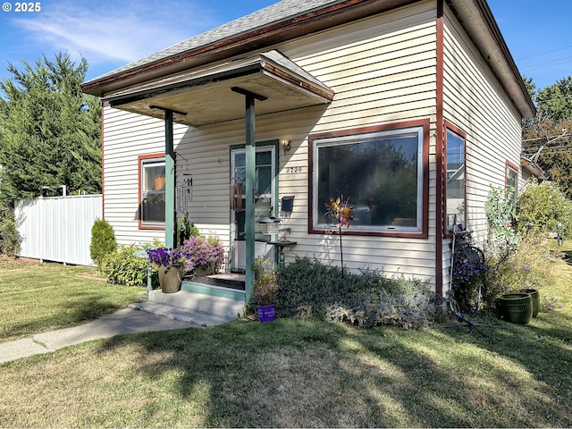 view of front of house with a shingled roof, a front yard, and fence