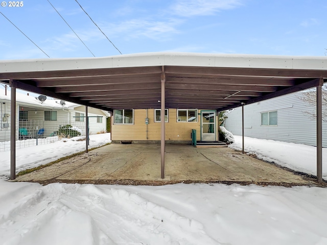 snow covered parking area featuring entry steps, a carport, and fence