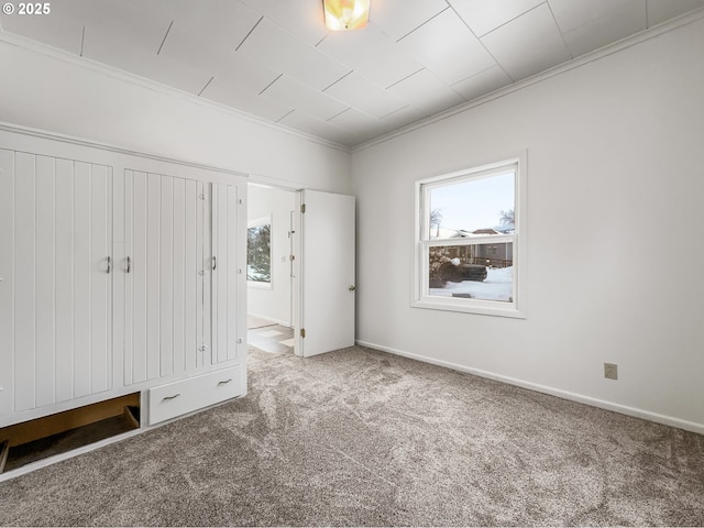 unfurnished bedroom featuring carpet, multiple windows, crown molding, and baseboards