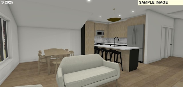 kitchen featuring backsplash, stainless steel fridge, decorative light fixtures, a kitchen island with sink, and light wood-type flooring