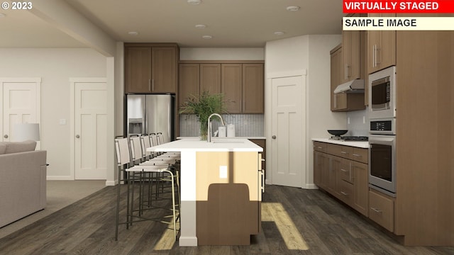 kitchen featuring sink, stainless steel appliances, an island with sink, a breakfast bar area, and backsplash