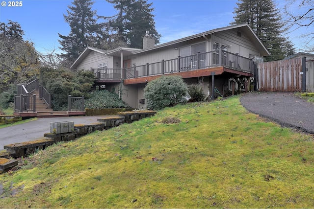 back of house featuring aphalt driveway, a wooden deck, stairs, a lawn, and a chimney