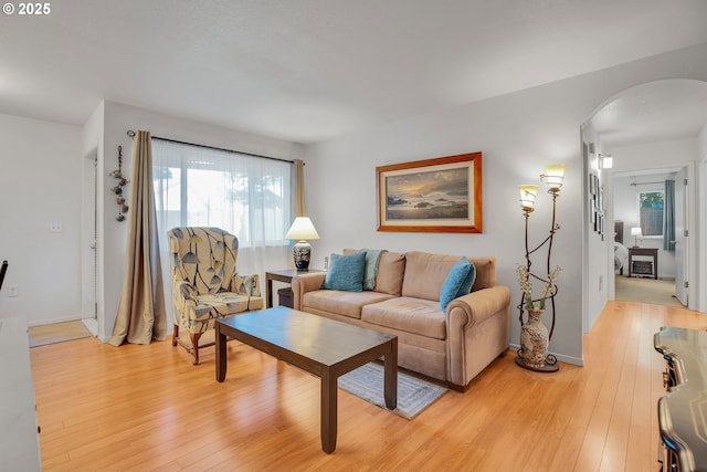 living room with arched walkways, light wood finished floors, and baseboards
