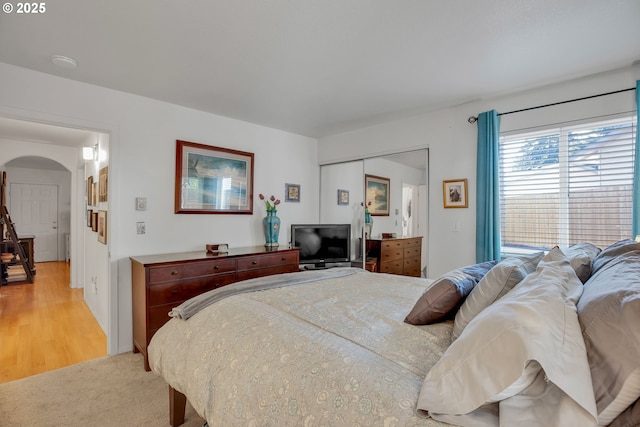 bedroom featuring arched walkways, a closet, light wood-style floors, and light carpet