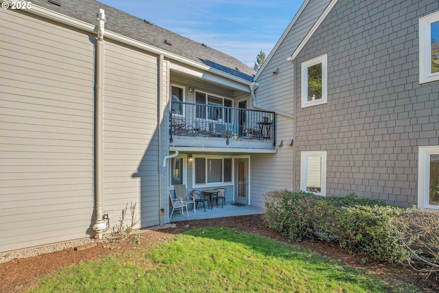 rear view of property with a balcony, a lawn, and a patio