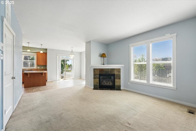unfurnished living room with light colored carpet, baseboards, and a tiled fireplace