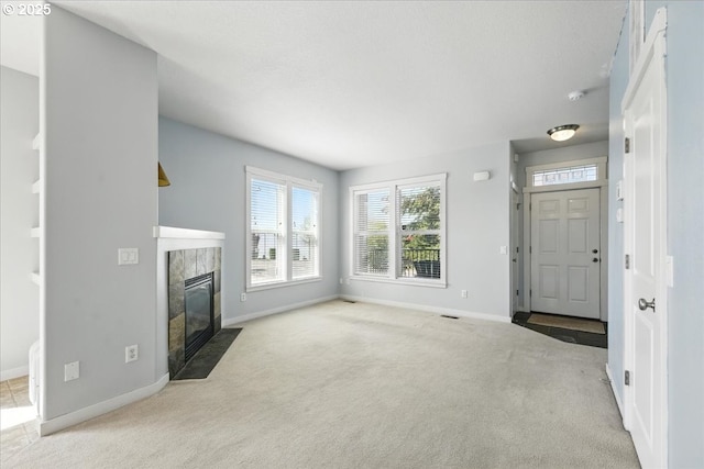 unfurnished living room featuring carpet, baseboards, and a tiled fireplace