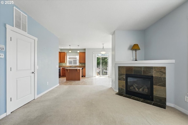 unfurnished living room featuring light colored carpet, baseboards, and a tiled fireplace