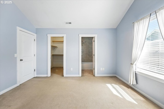 unfurnished bedroom featuring carpet flooring, baseboards, a spacious closet, vaulted ceiling, and ensuite bath