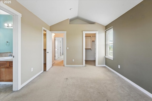 unfurnished bedroom featuring vaulted ceiling, a sink, a walk in closet, light colored carpet, and baseboards
