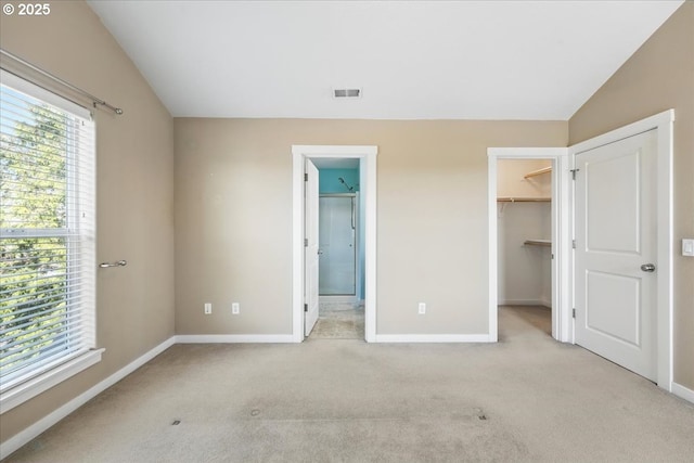 unfurnished bedroom with vaulted ceiling, a walk in closet, light colored carpet, baseboards, and a closet