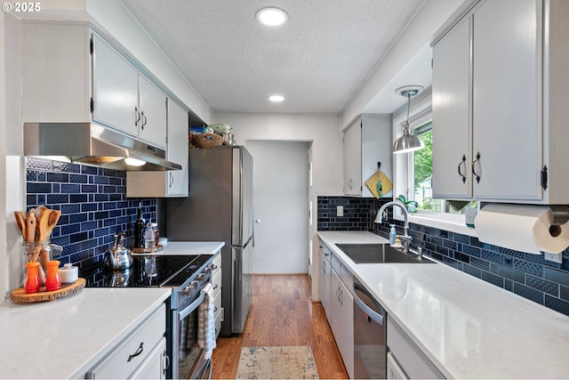 kitchen featuring a textured ceiling, appliances with stainless steel finishes, a sink, light countertops, and under cabinet range hood