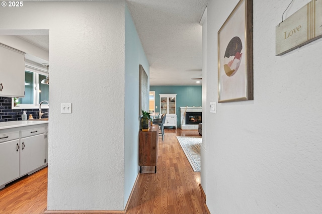 hallway featuring a textured wall, a sink, and light wood-style flooring