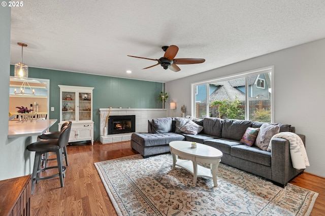 living area with wood finished floors, a fireplace, ceiling fan, recessed lighting, and a textured ceiling