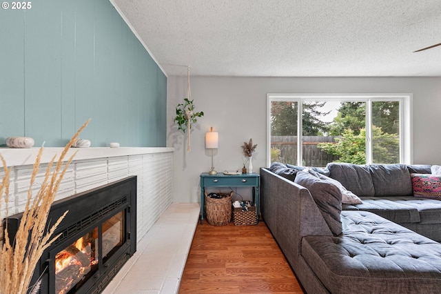 living area featuring a ceiling fan, a textured ceiling, a glass covered fireplace, and wood finished floors