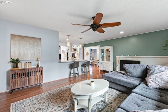 living area featuring a brick fireplace, a ceiling fan, and wood finished floors