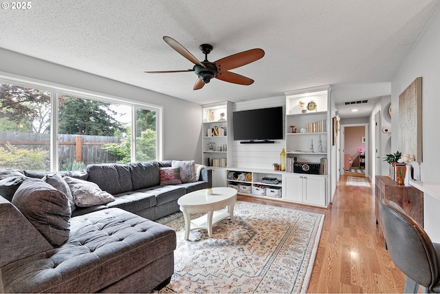 living area with a ceiling fan, a textured ceiling, visible vents, and light wood-type flooring