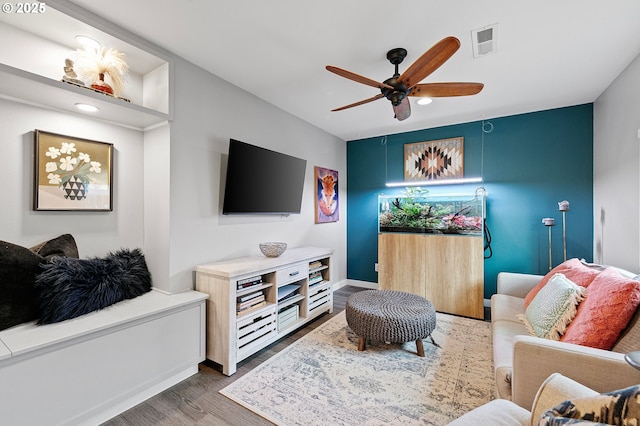 living room featuring visible vents, a ceiling fan, baseboards, and wood finished floors