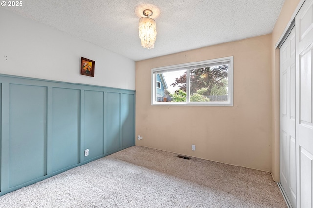 unfurnished bedroom with a textured ceiling, visible vents, carpet floors, a wainscoted wall, and a decorative wall