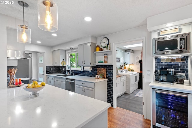 kitchen featuring appliances with stainless steel finishes, open shelves, washing machine and dryer, a sink, and beverage cooler
