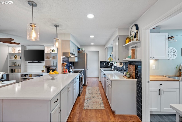 kitchen with open shelves, a sink, stainless steel stove, light countertops, and light wood-type flooring
