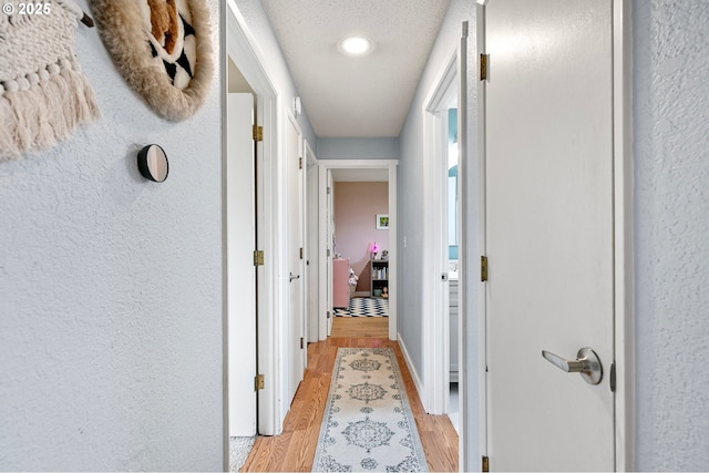 hall featuring baseboards, a textured wall, and light wood finished floors