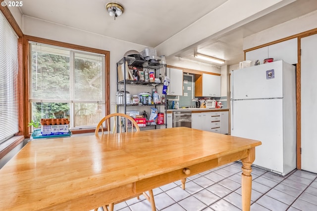 kitchen with light tile patterned floors, tasteful backsplash, white cabinets, freestanding refrigerator, and a sink