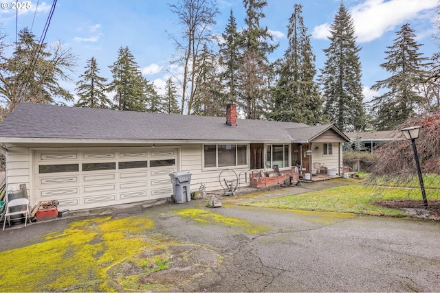 view of front of home featuring an attached garage, driveway, roof with shingles, a chimney, and a front yard