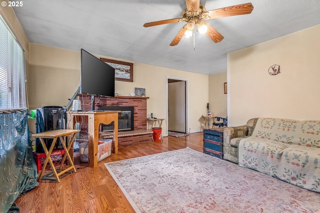 living area with a ceiling fan, a brick fireplace, a textured ceiling, and wood finished floors