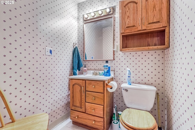 bathroom with toilet, wallpapered walls, vanity, and tile patterned floors