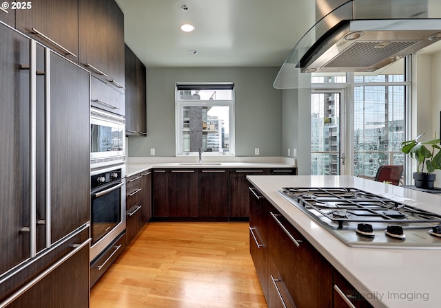 949 NW Overton St Unit 1302, Portland, OR 97209 - kitchen featuring range hood, built in appliances, light countertops, light wood finished floors, and dark brown cabinetry