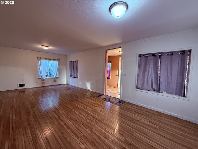 unfurnished living room with baseboards, visible vents, and wood finished floors