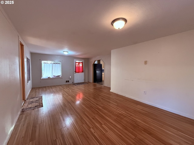 unfurnished living room featuring arched walkways, baseboards, visible vents, and wood finished floors