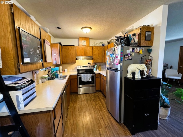 kitchen with brown cabinetry, dark wood-style floors, stainless steel appliances, light countertops, and a sink