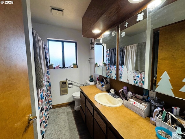 full bathroom with heating unit, visible vents, toilet, vanity, and baseboards