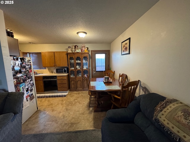 kitchen featuring a textured ceiling, black dishwasher, light countertops, freestanding refrigerator, and stainless steel microwave