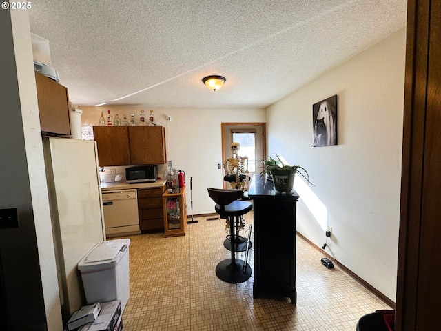 kitchen with baseboards, stainless steel microwave, white dishwasher, light countertops, and a textured ceiling