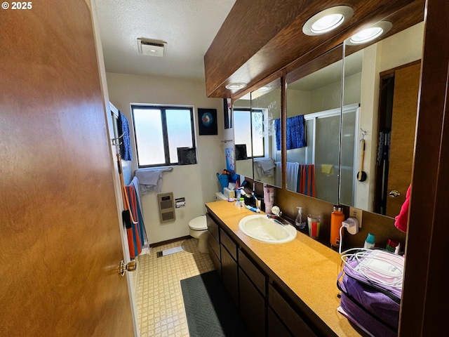 bathroom with toilet, vanity, visible vents, heating unit, and a stall shower