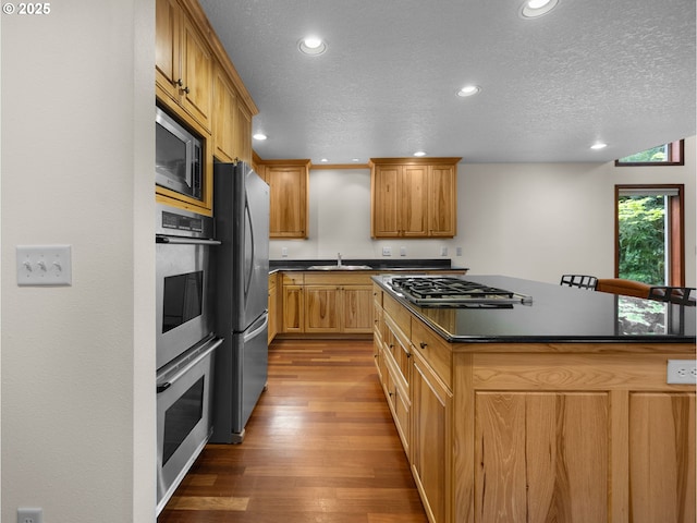 24982 E Tillicum St, Welches, OR 97067 - kitchen featuring stainless steel appliances, dark countertops, a sink, wood finished floors, and recessed lighting