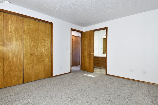 unfurnished bedroom featuring carpet floors, baseboards, a closet, a textured ceiling, and ensuite bath