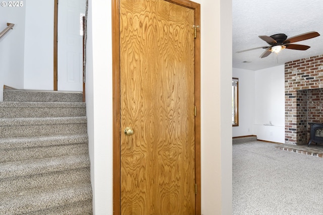 stairway featuring a wood stove, ceiling fan, carpet, a textured ceiling, and baseboards